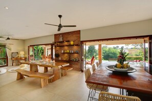 A spacious dining area with a long wooden table, benches, and a view of lush greenery outside. - Villa Subak (Canggu)