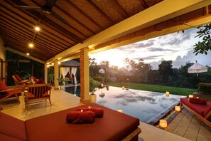A serene indoor pool area with a wooden ceiling, red seating, and a view of the outdoors. - Villa Subak (Canggu)