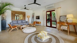 Un salon spacieux avec un canapé gris, des chaises en bois, un tapis rond et un ventilateur de plafond.