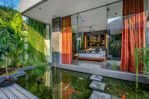 A modern bedroom with a glass wall, a bed with pillows, and a painting. - Villa Banyu (Seminyak)