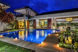 Una casa moderna con piscina, terraza de madera y espacios de estar integrados, tanto interiores como exteriores.