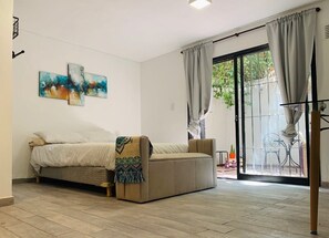 Une pièce comprenant un lit, un canapé, une porte-fenêtre coulissante donnant sur un espace extérieur et des œuvres d’art abstraites accrochées au mur.