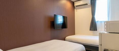 A hotel room with two beds, a flat-screen TV mounted on the wall, an air conditioning unit, a microwave, and a window with curtains.