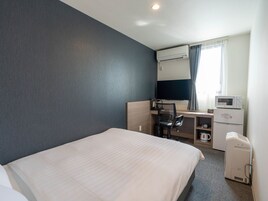 Habitación de hotel con cama, escritorio, silla, microondas, cafetera y televisión.