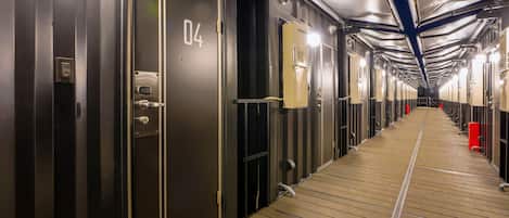 Un pasillo con puertas numeradas que dan a habitaciones individuales, suelo de madera e iluminación en el techo.