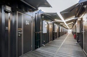 Un pasillo con puertas numeradas que dan a habitaciones individuales, suelo de madera e iluminación en el techo.