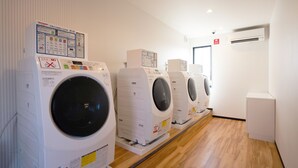 A row of white front-loading washing machines in a laundry room with wooden flooring and white walls. - HOTEL R9 The Yard Ota (Ota)