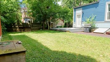 A backyard with a wooden deck, a small shed, and a blue house.