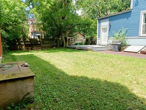 A backyard with a wooden deck, a small shed, and a blue house.
