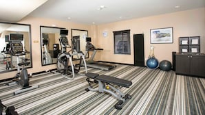 Ginásio com equipamentos de exercício, um banco, esteiras e um espelho grande.