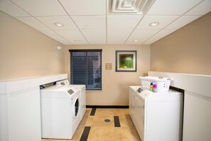 A laundry room with two washing machines, a window with blinds, and a framed picture on the wall. - Candlewood Suites Jacksonville - Mayport (Atlantic Beach)