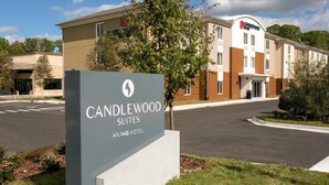 Señal de hotel para Candlewood Suites, parte de la cadena IHG Hotel, con una carretera despejada y vegetación al frente.