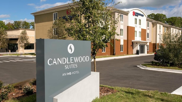 Placa de hotel para Candlewood Suites, parte da cadeia de hotéis IHG, com uma estrada visível e vegetação ao primeiro plano.