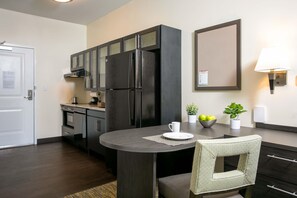A modern kitchen with dark cabinetry, a built-in refrigerator, and a round dining table with a chair.