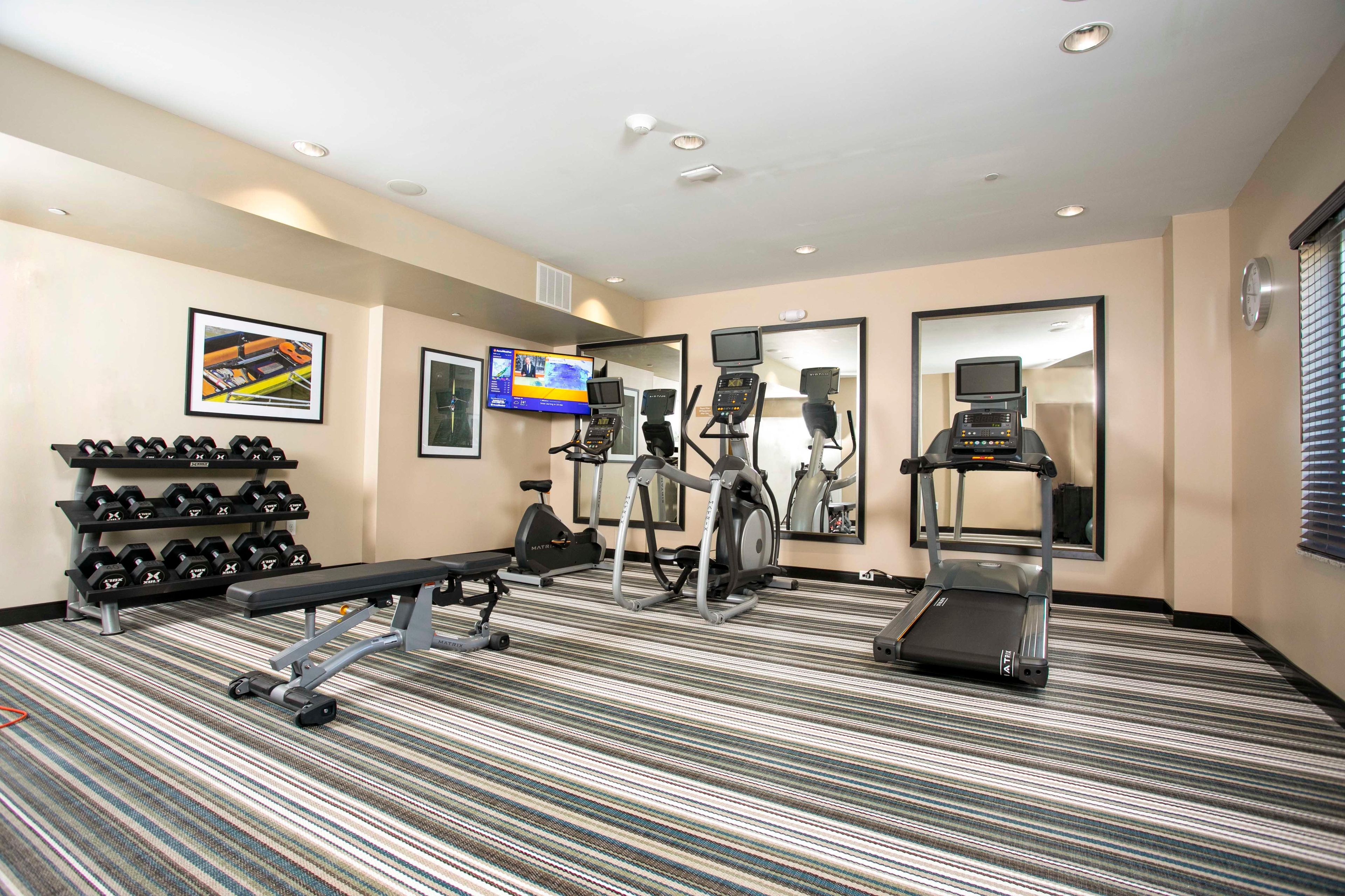 Une salle de sport d’hôtel équipée d’un tapis de course, d’un vélo elliptique et d’un banc de musculation.