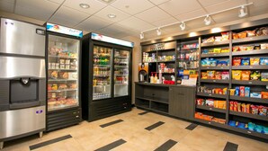 Un espacio autoservicio con refrigerios y bebidas, que incluye congeladores, estantes llenos de bocadillos y un dispensador de agua.