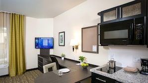 Habitación de hotel con una mesa de comedor, microondas, cafetera y televisión mostrando un pronóstico del tiempo.