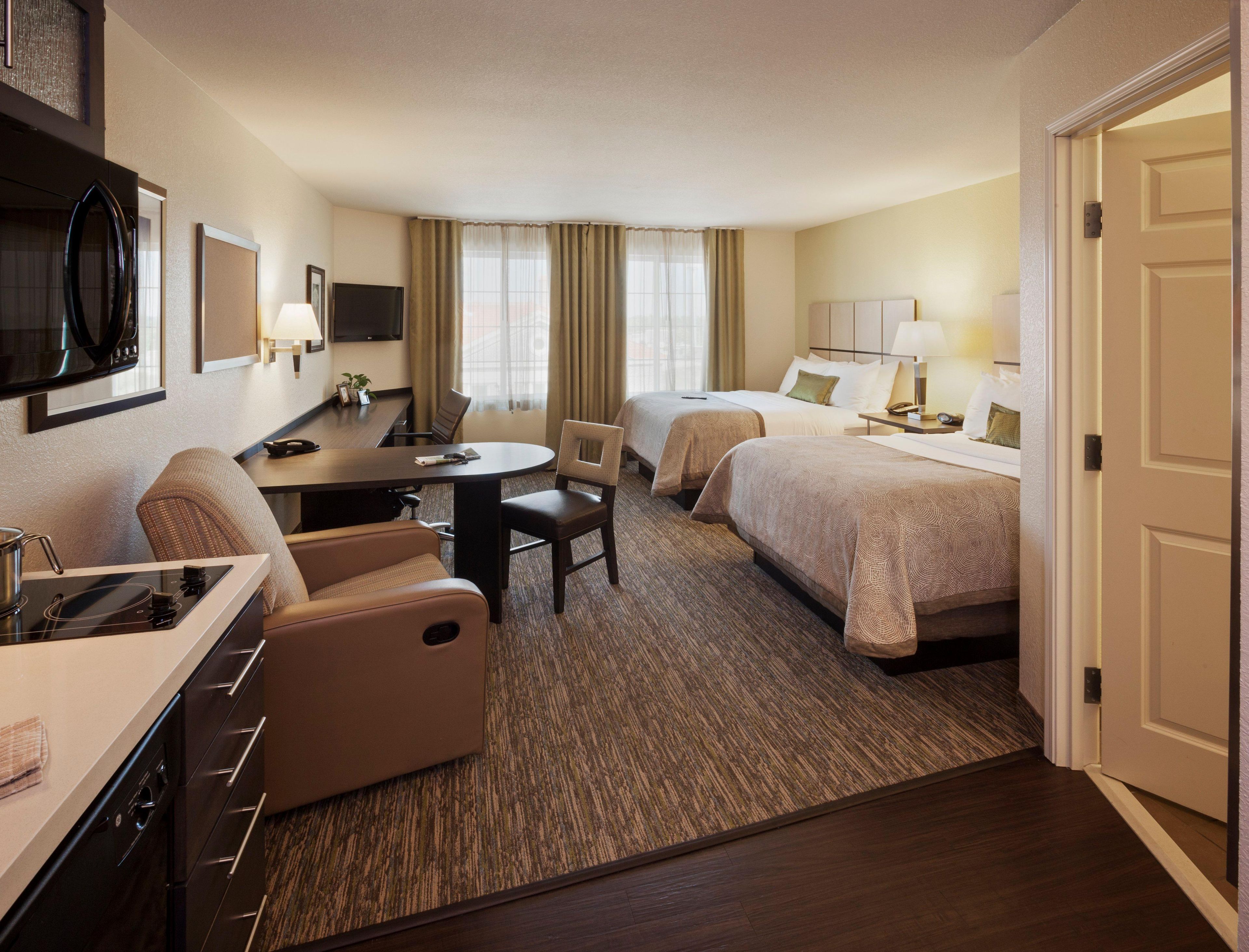 A hotel room with a kitchenette, two beds, a dining table, and a TV.