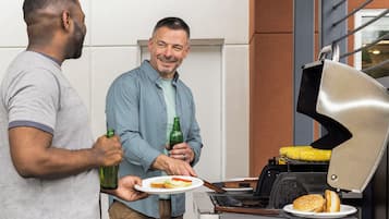 Two people near a grill with a plate of food and a bottle.