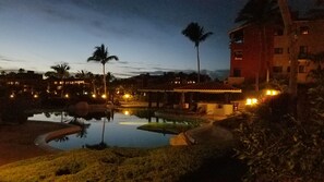 A nighttime view of a resort with a swimming pool, palm trees, and illuminated buildings.