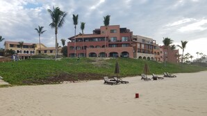 A beachfront hotel with multiple balconies, palm trees, and sun loungers on the sandy beach. - Casa Del Mar Beachnest (San José del Cabo)