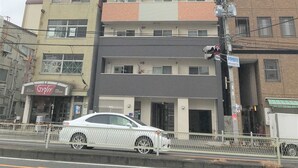 Ein mehrstöckiges Gebäude mit einer Mischung aus Backstein- und Betonfassaden, ein sichtbares Schaufenster mit einem Zigeunercafé und ein weißes Auto davor geparkt.