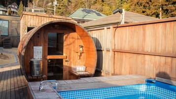 A wooden sauna with a glass door, a wooden bench, and a small table.