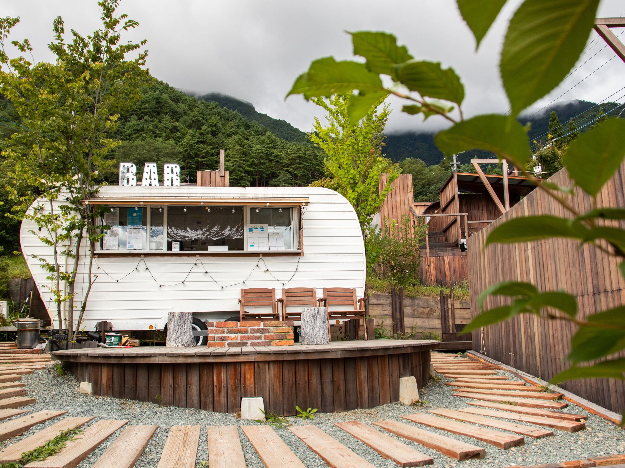 A white RV with a wooden deck, surrounded by a wooden fence and gravel paths.