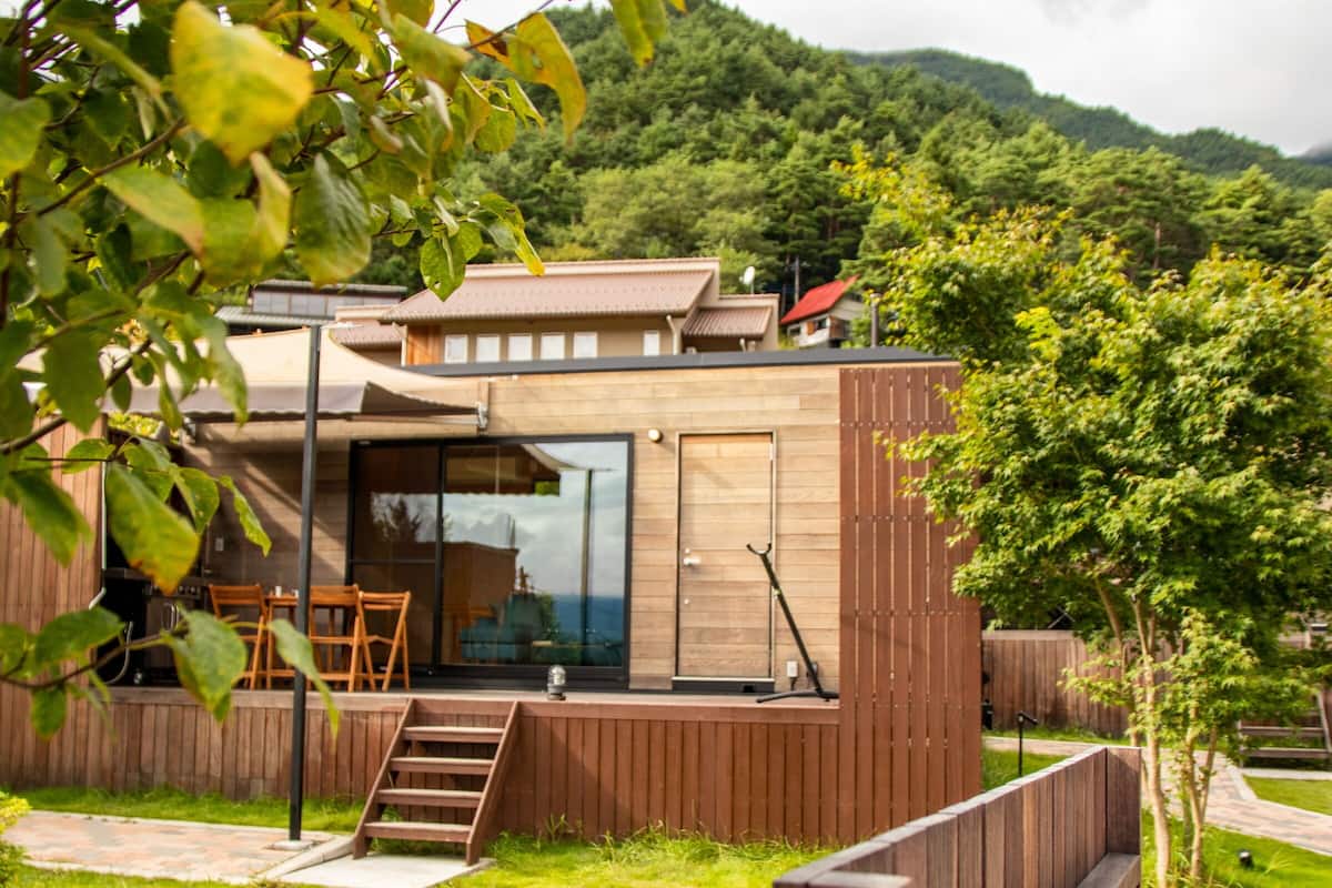 Una casa moderna con terraza de madera, puerta de cristal y vistas a una colina boscosa.