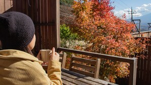 A person sitting at a wooden table outdoors, holding a cup. - Dot Glamping Fujisan (Fujikawaguchiko)