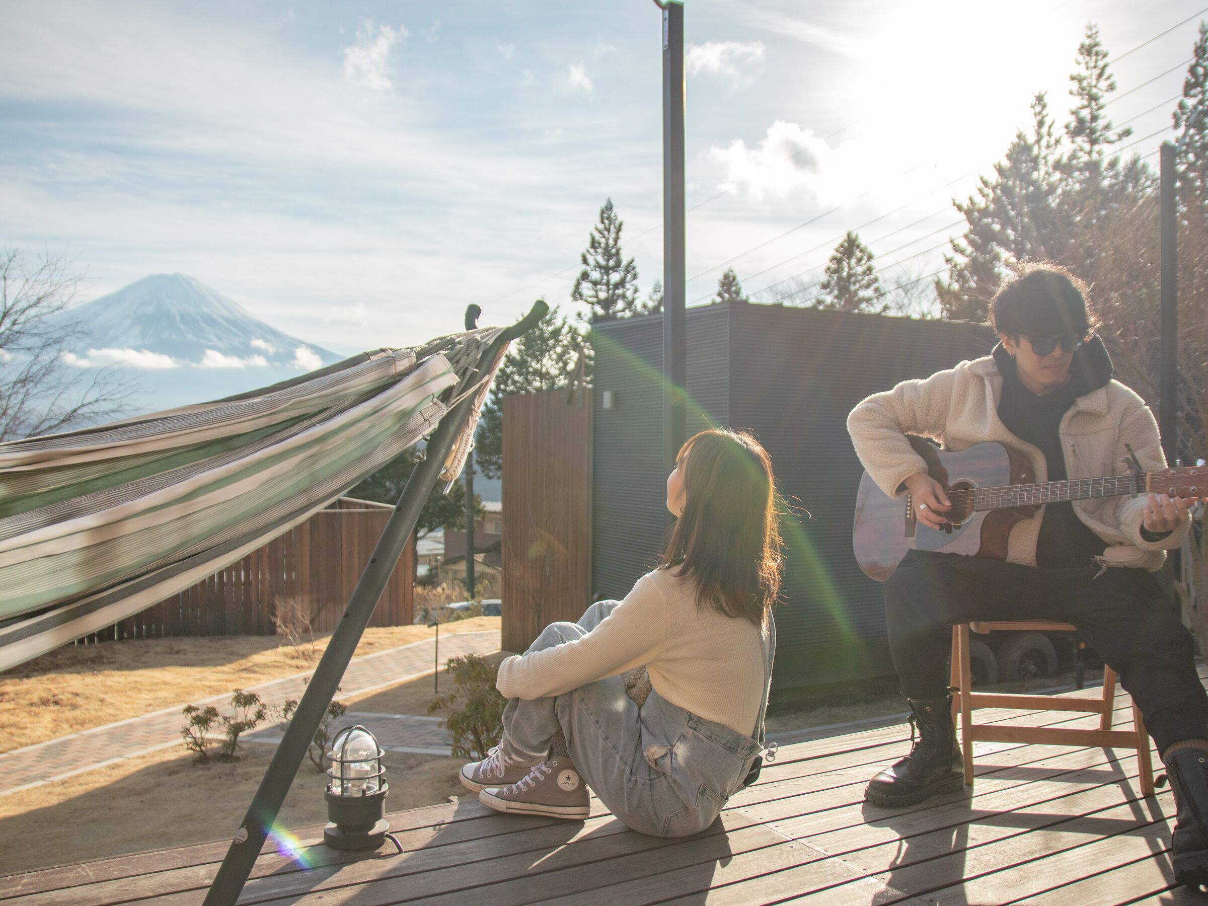 A hammock, a person playing guitar, and another person sitting on the deck.