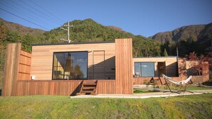 A modern wooden cabin with large windows, a wooden deck, and a hammock. - Dot Glamping Fujisan (Fujikawaguchiko)