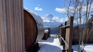 A snow-covered outdoor area with wooden barrels, a wooden fence, and a mountain in the background. - Dot Glamping Fujisan (Fujikawaguchiko)