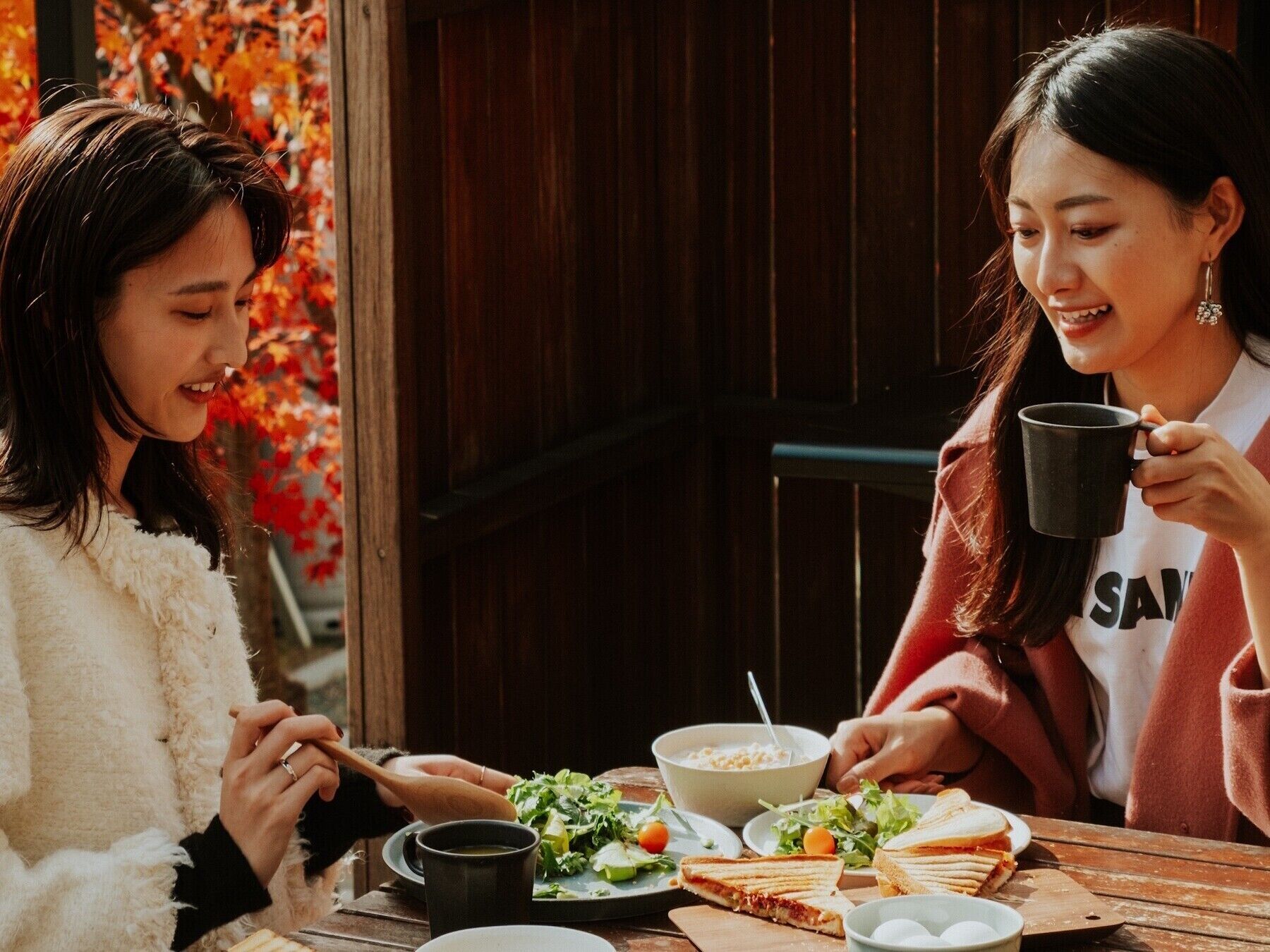 Two people dining at a wooden table with a salad, sandwiches, and a bowl of soup.