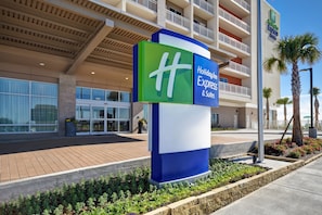 Ein Holiday Inn Express Gebäude mit auffälligem Schild, großen Fenstern und einer begrünten Anlage mit Pflanzen und einer Palme.