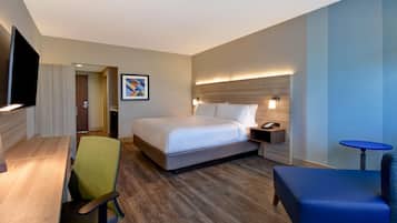 A hotel room with a bed, a desk, a chair, a TV, a bedside table, and a small table.