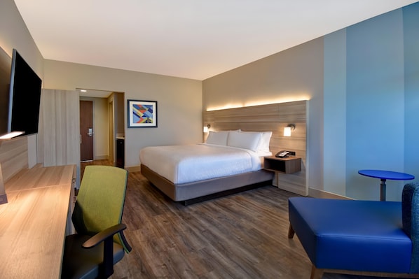 A hotel room with a bed, a desk, a chair, a TV, a bedside table, and a small table. - Holiday Inn Express And Suites Galveston Beach (Galveston)