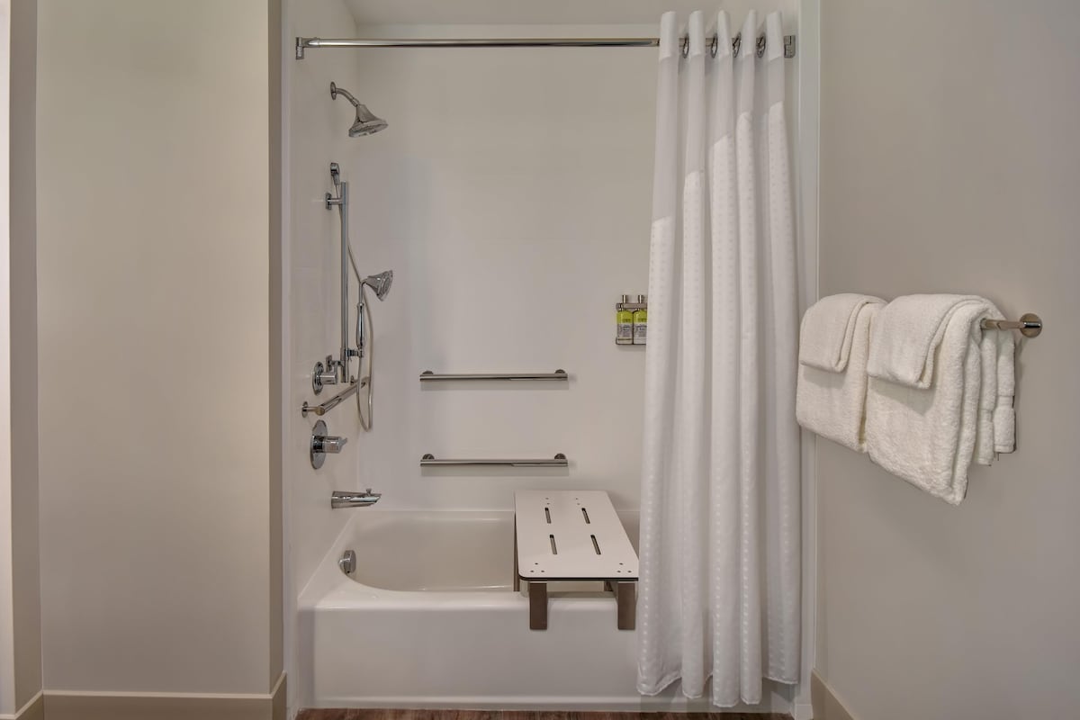Eine bodenebene Dusche mit Badewanne, Duschkopf, Handbrause, Handtuchhalter und einer kleinen Stehgehocker.