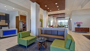 A modern lobby with green upholstered sofas, a reception desk, a refrigerator stocked with snacks, and a seating area with a patterned sofa and a small table. - Holiday Inn Express And Suites Galveston Beach (Galveston)