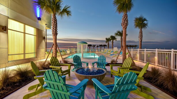 A poolside area with Adirondack chairs, a fire pit, and palm trees. - Holiday Inn Express And Suites Galveston Beach (Galveston)