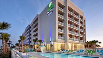 Een Holiday Inn Express gebouw met een zwembad, inclusief ligbedden en palmbomen.