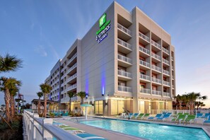 Un bâtiment de l’hôtel Holiday Inn Express doté d’un espace piscine, comprenant des chaises longues et des palmiers.