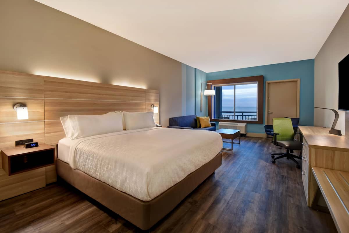 Ein Hotelzimmer mit einem großen Bett, Nachttischen, einem Schreibtisch, einem Sessel und Meerblick.