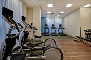 Une salle de sport équipée de tapis de course, de vélos elliptiques et d’une zone dédiée aux exercices de développé couché.