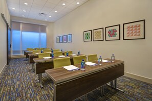Une salle de conférence équipée de tables, de chaises, de bouteilles d’eau et ornée d’œuvres d’art encadrées aux murs.