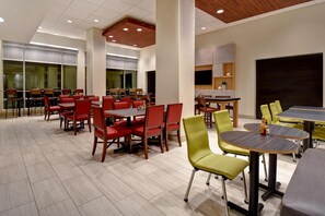 A modern dining area with multiple tables and chairs, large windows, and a kitchen area. - Holiday Inn Express And Suites Galveston Beach (Galveston)