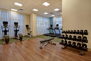 Academia com esteiras, elípticos, aparelho de supino e uma gama de halteres.