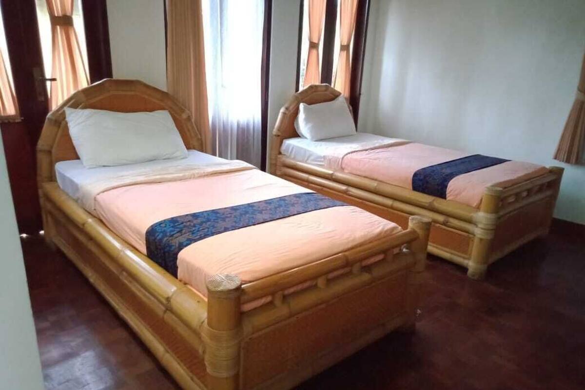 Twee houten bedden met hoofdborden, een raam met gordijnen en een houten vloer.