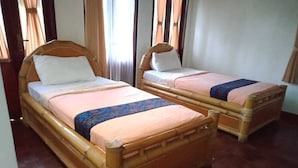 Dos camas de madera con cabeceras, una ventana con cortinas y piso de madera.