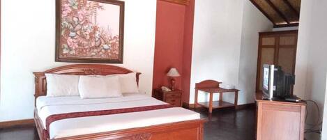 A bedroom with a large bed, a small table, a television, and a framed artwork on the wall.